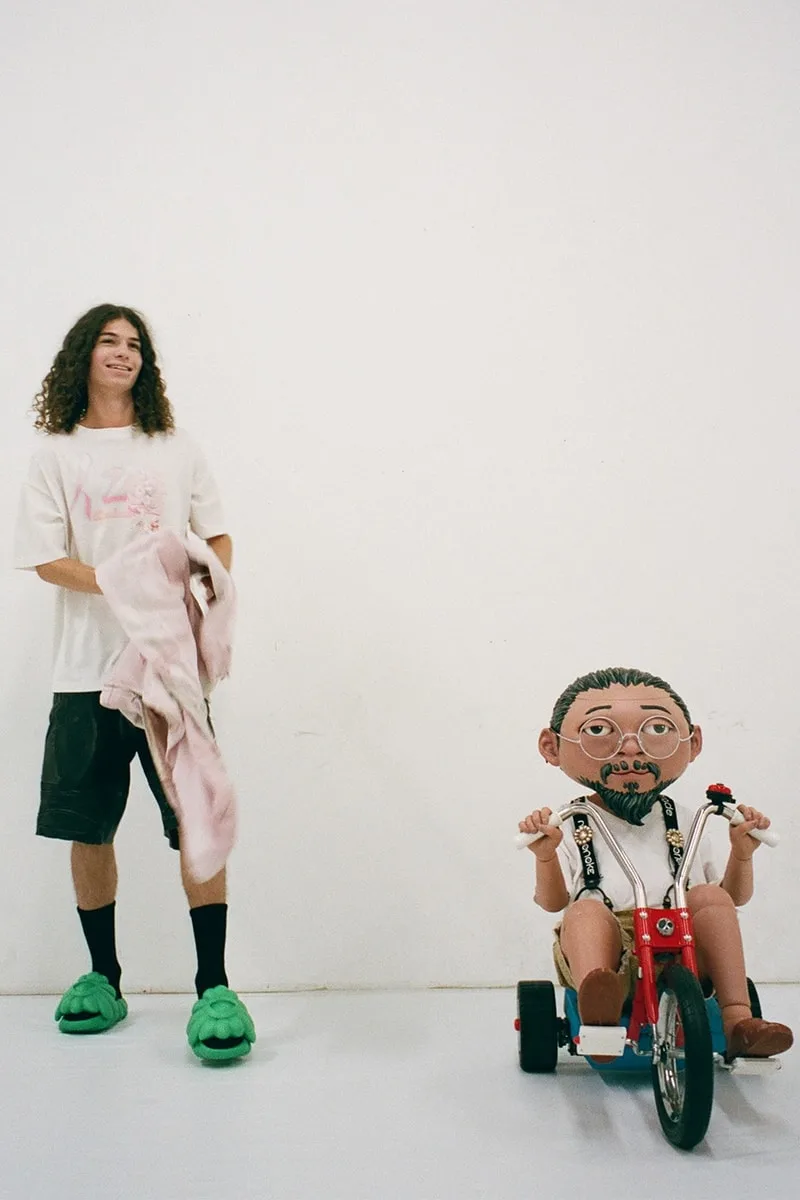 Un jeune homme et une grande figurine sur un tricycle dans une pièce vide.