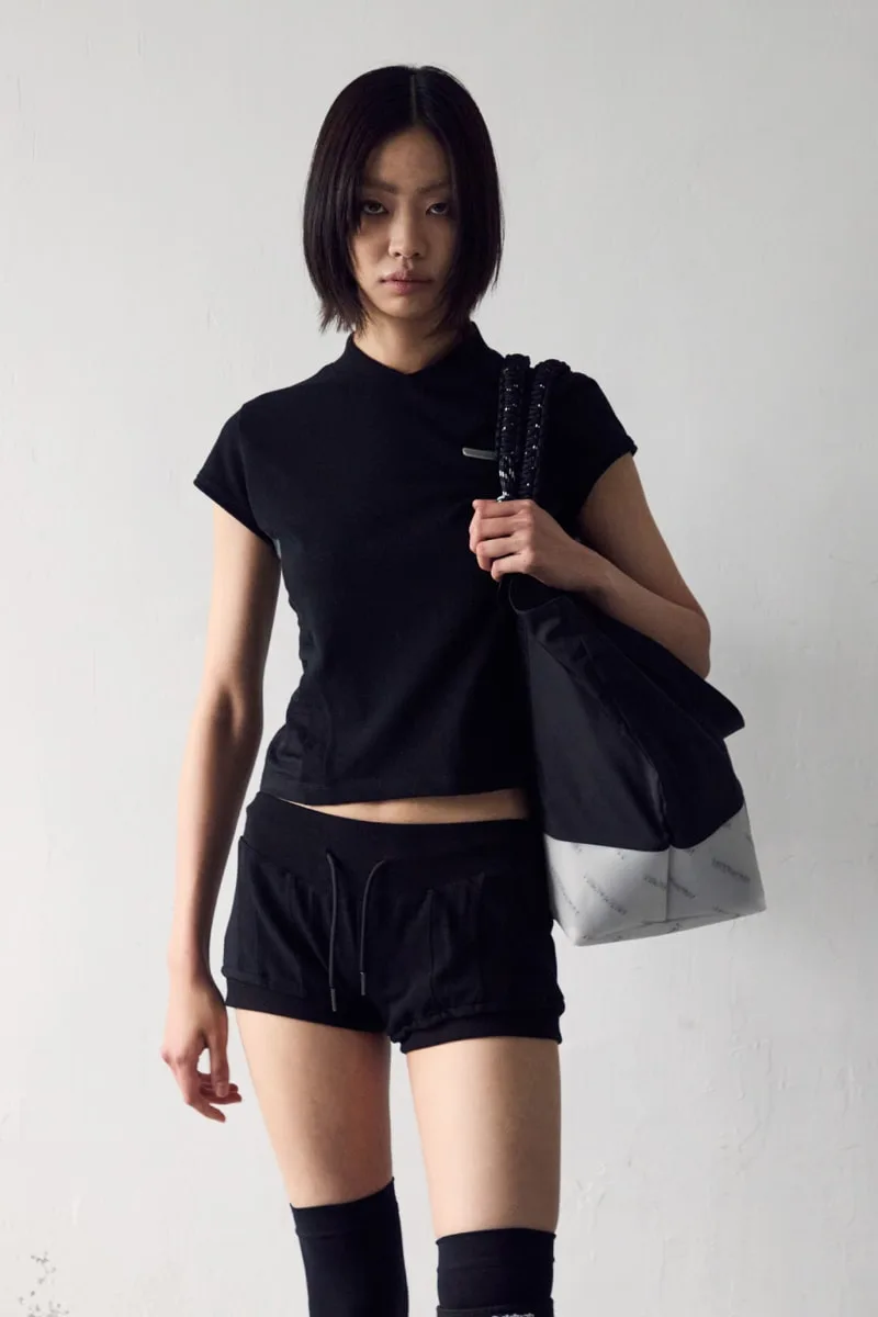 Femme en tenue sportive noire, sac sur l'épaule, pose neutre.