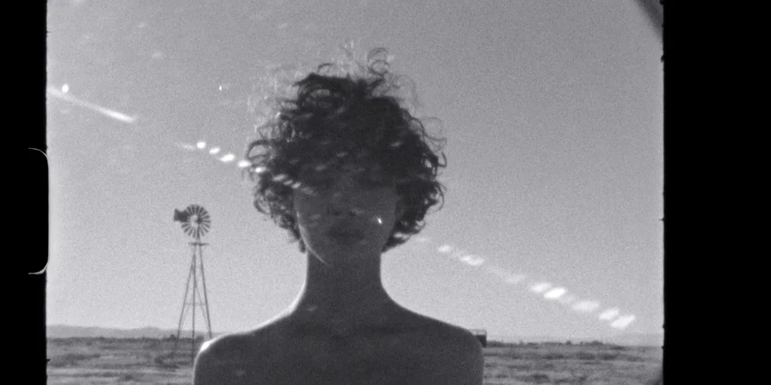 Personne aux cheveux bouclés devant un paysage désertique.