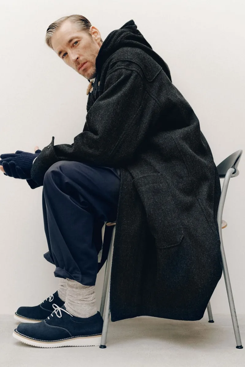 Homme assis avec manteau long, chaussettes et chaussures élégantes.
