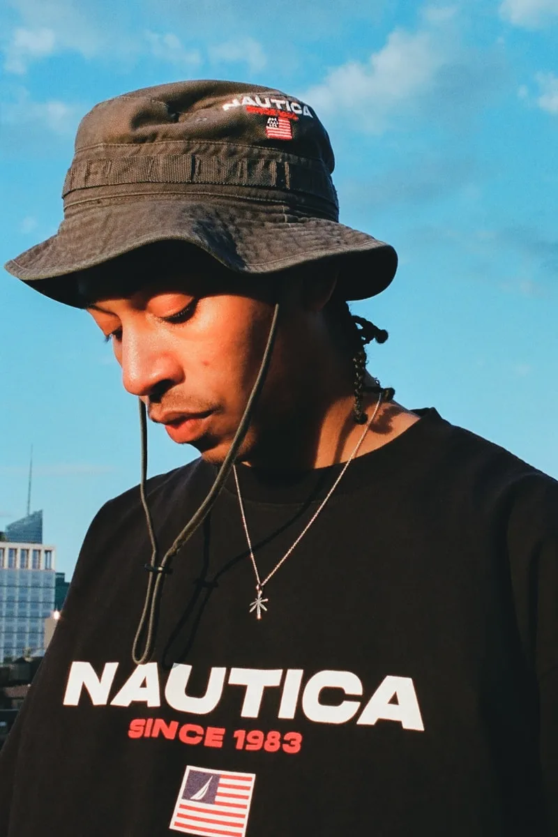 Homme avec chapeau et t-shirt Nautica devant ciel bleu.