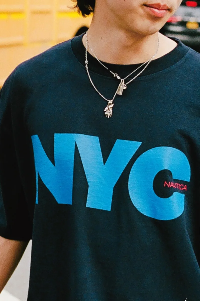 Homme portant un t-shirt noir avec 'NYC' en lettres bleues.