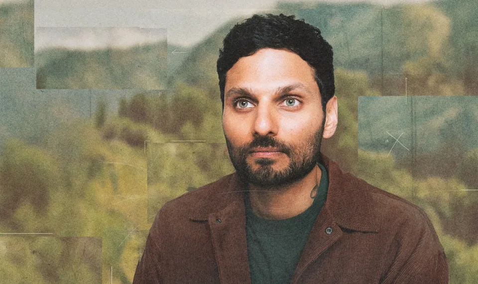 Homme avec barbe devant paysage flou de montagnes.