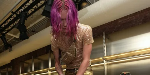 Personne aux cheveux roses vêtue d'une tenue brillante dans un environnement industriel.