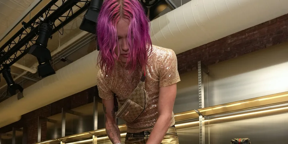 Personne aux cheveux roses vêtue d'une tenue brillante dans un environnement industriel.