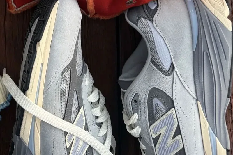 Deux baskets New Balance blanches et grises posées sur du bois.
