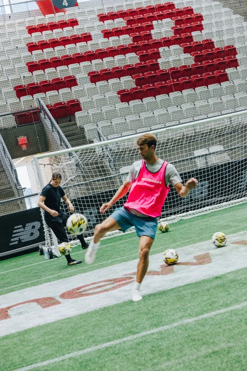 Deux personnes jouent au football en salle, l'une tirant un ballon.