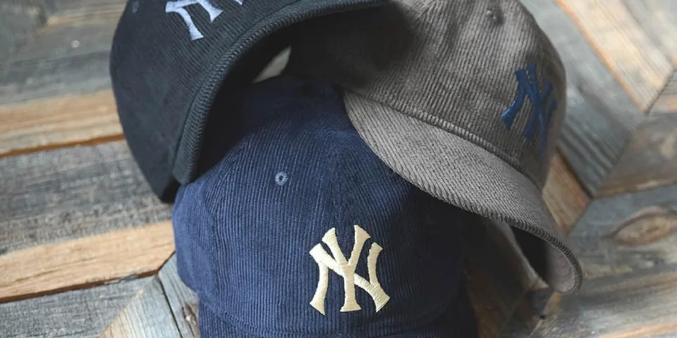 Trois casquettes avec logo stylisé, disposées sur une surface en bois.