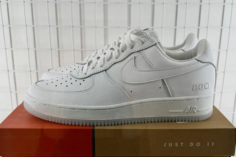 Chaussures blanches Nike Air Force 1 sur boîte orange, grille en fond.