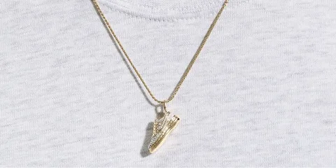 Collier avec pendentif chaussure en or sur t-shirt blanc.