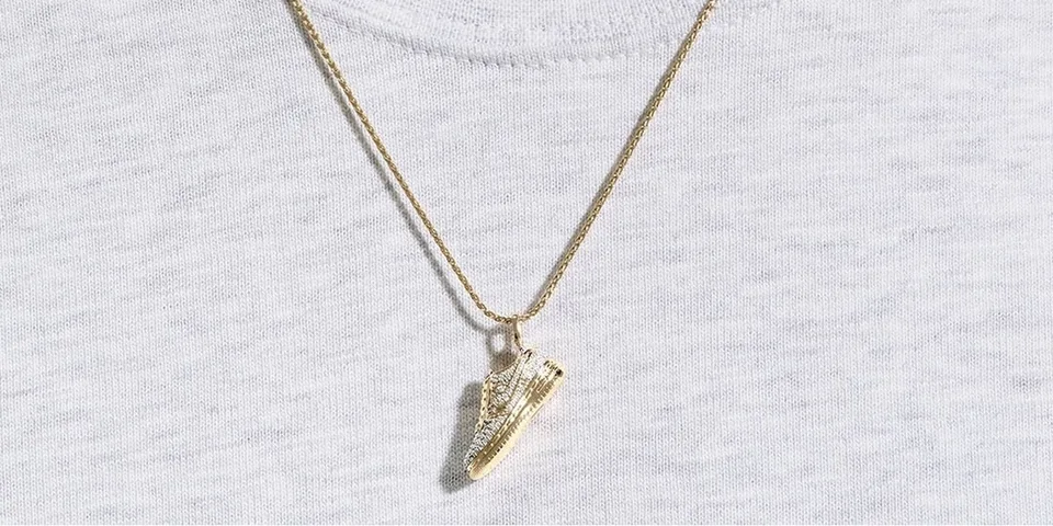 Collier avec pendentif chaussure en or sur t-shirt blanc.