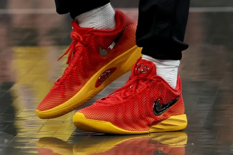 Chaussures Nike rouges et jaunes avec logo noir, sur un sol sombre.