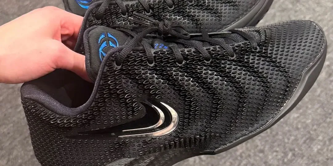 Main tenant des baskets noires avec un logo argenté et bleu.
