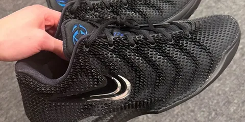 Main tenant des baskets noires avec un logo argenté et bleu.