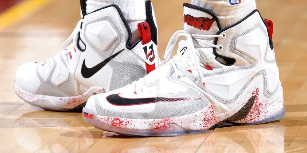 Chaussures de sport blanches avec motif noir et rouge sur un sol de basketball.