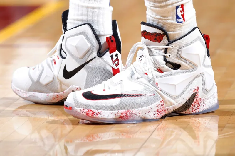 Baskets blanches avec éclaboussures rouges sur un terrain de basket.