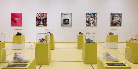 Exposition de chaussures et photos dans une galerie lumineuse avec socles jaunes.
