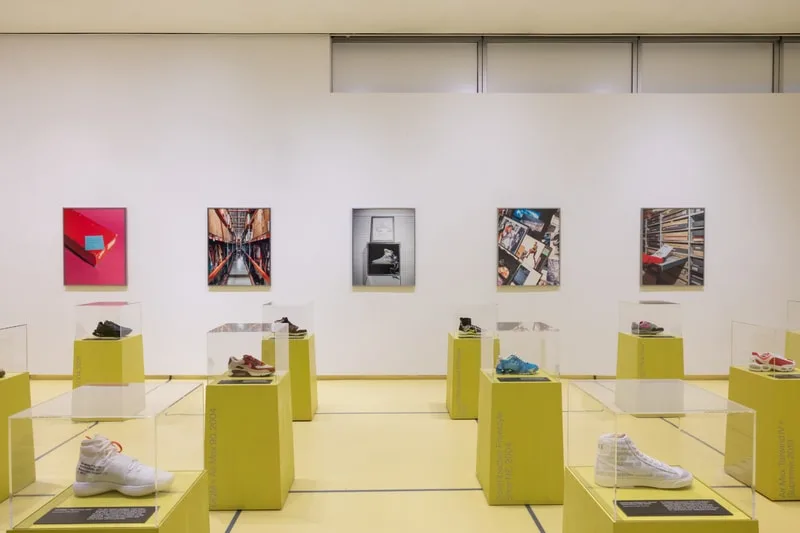 Exposition de chaussures modernes sur des socles jaunes avec des photos en arrière-plan.