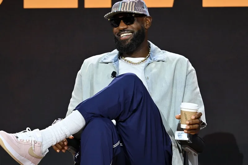 Homme souriant portant des lunettes de soleil, assis avec un café.