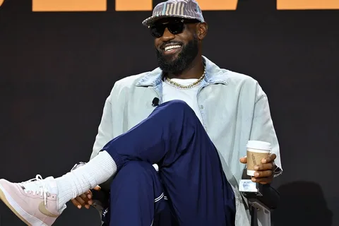 Homme souriant portant des lunettes de soleil, assis avec un café.