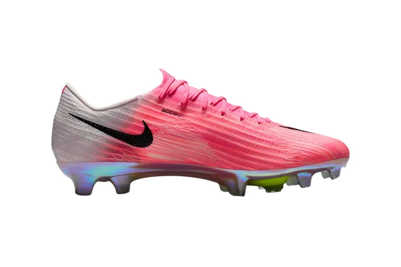 Chaussure de football rose avec logo noir et semelle irisée.