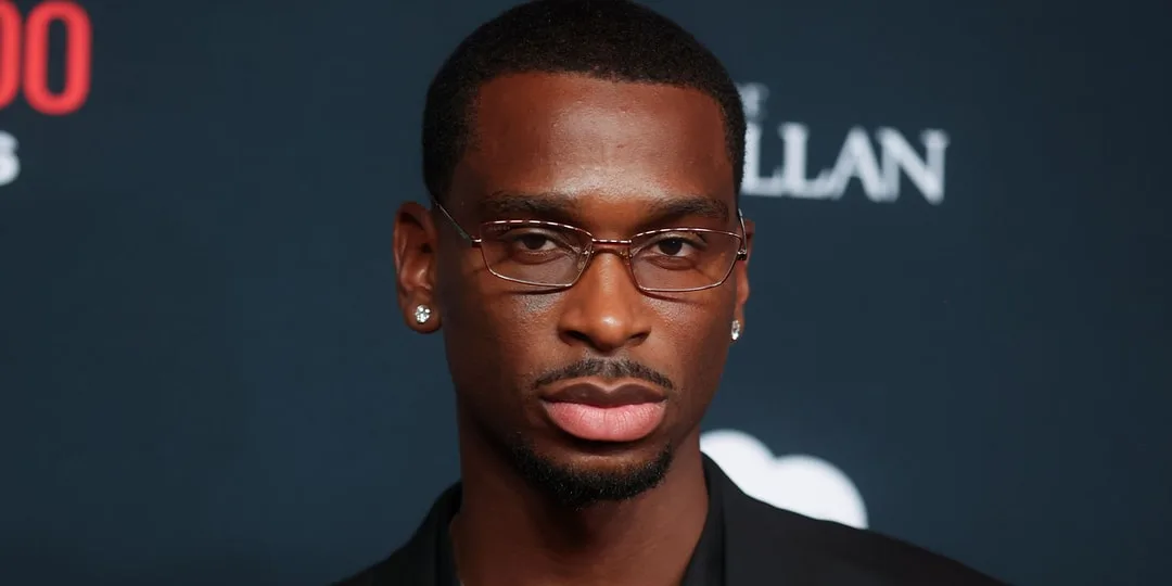Homme avec lunettes et boucle d'oreille sur fond noir.