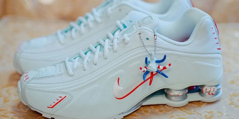 Paire de baskets blanches avec des détails rouges et bleus, et un pendentif.