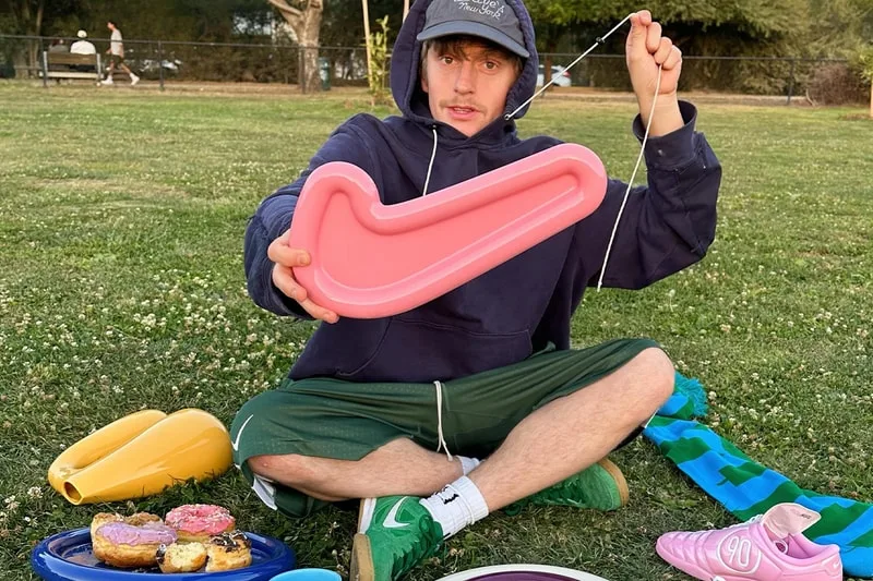 Homme assis dans un parc tenant un objet rose en forme de logo Nike.