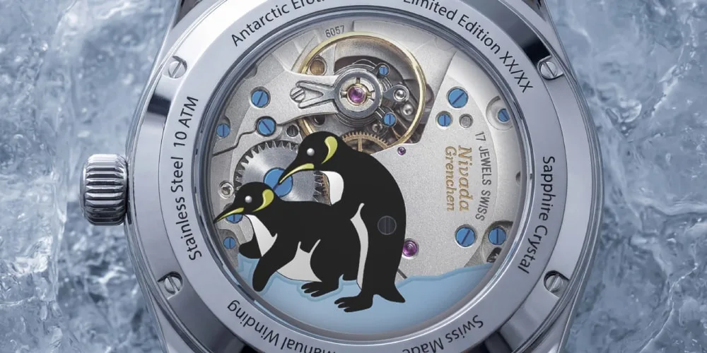 Montre avec fond transparent, deux manchots sur fond de mécanisme visible.