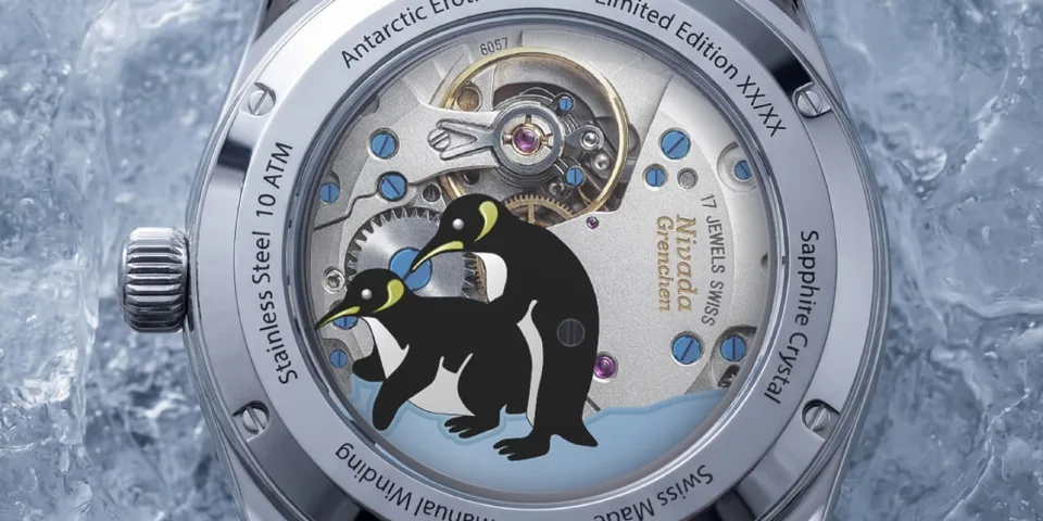 Montre avec fond transparent, deux manchots sur fond de mécanisme visible.