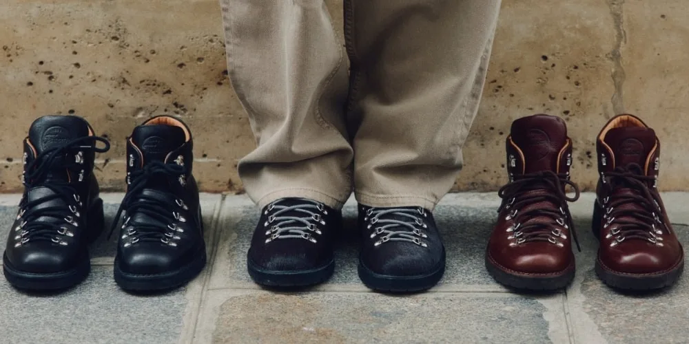 Trois paires de bottes de randonnée à côté d'une personne portant un pantalon beige.