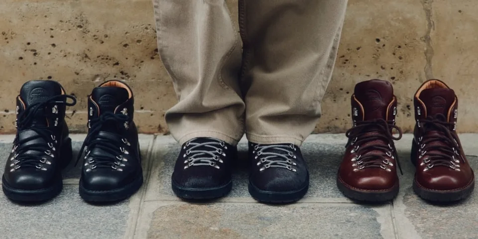 Trois paires de bottes de randonnée à côté d'une personne portant un pantalon beige.