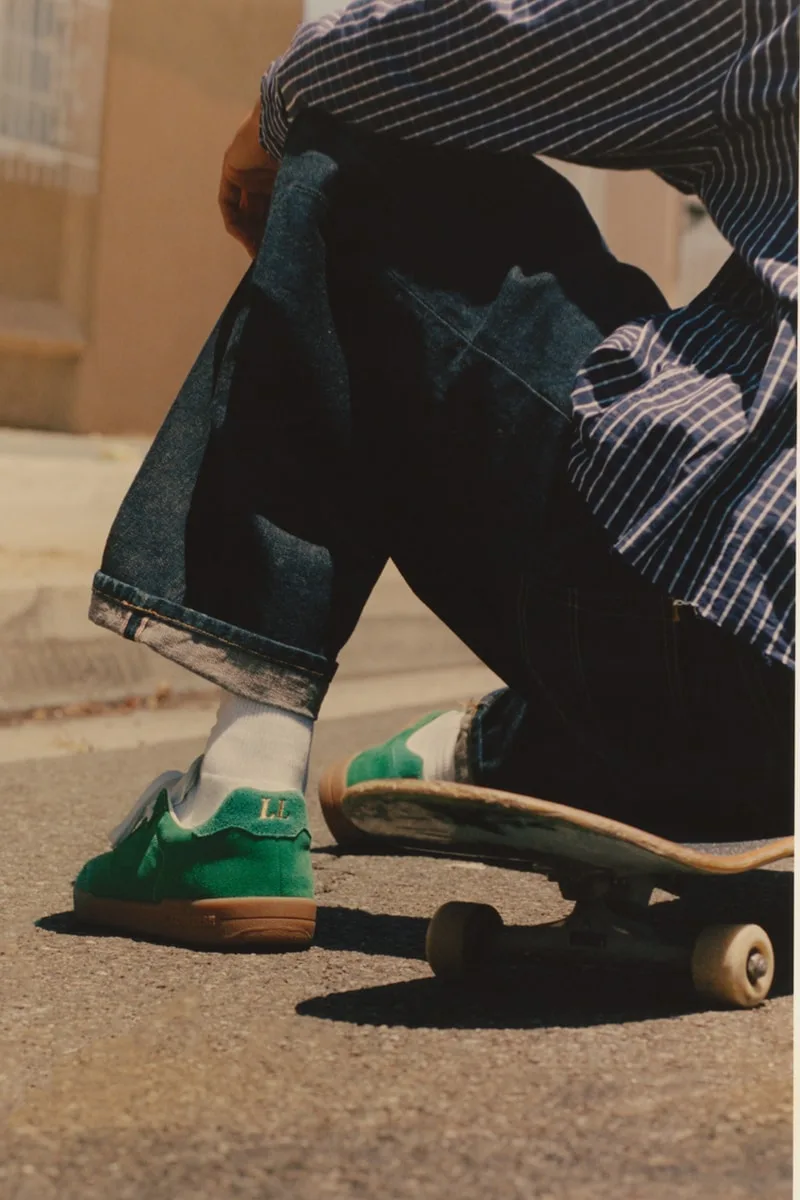 Personne assise sur un skateboard portant des baskets vertes et un jean.