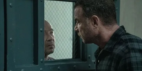 Deux hommes se font face à travers une fenêtre grillagée.