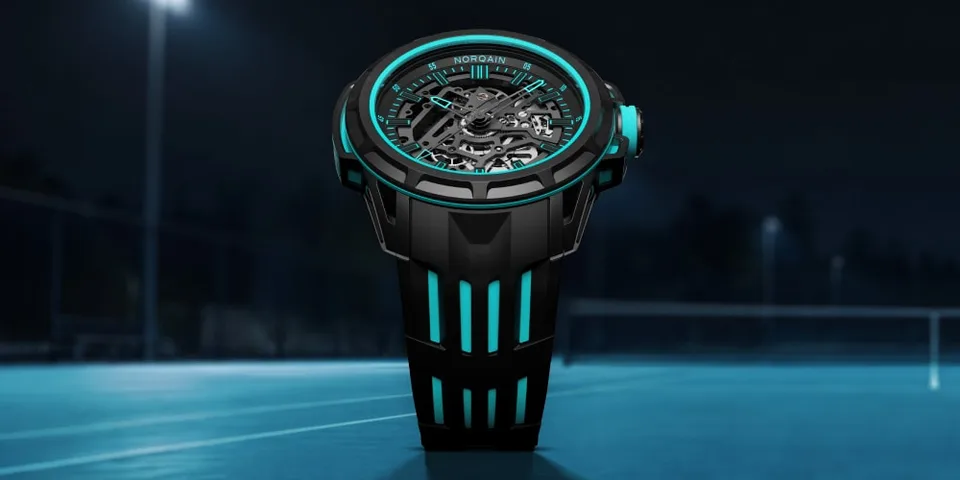 Montre noire et turquoise au cadran mécanique, posée sur une surface bleue.