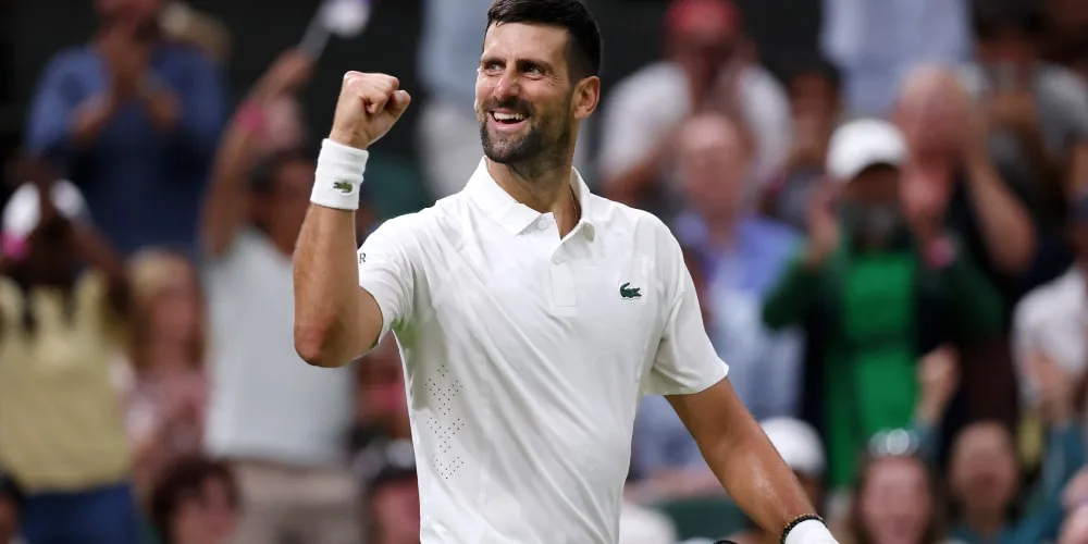 Homme en tenue de tennis blanc levant le poing, foule floue en arrière-plan.