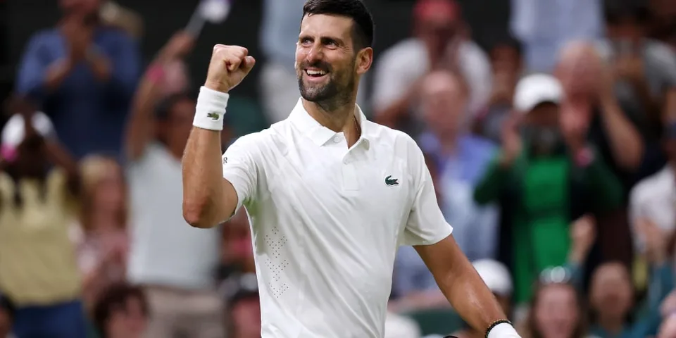 Homme en tenue de tennis blanc levant le poing, foule floue en arrière-plan.