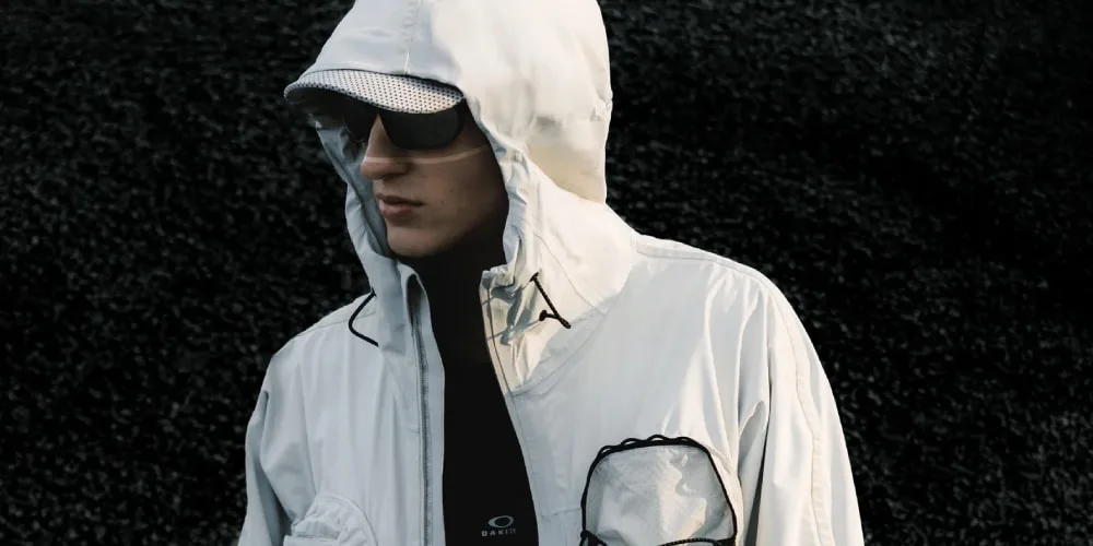 Personne en veste blanche avec capuche et lunettes noires, fond noir.