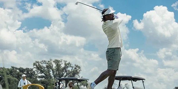 Un golfeur frappant une balle sous un ciel bleu avec des nuages.