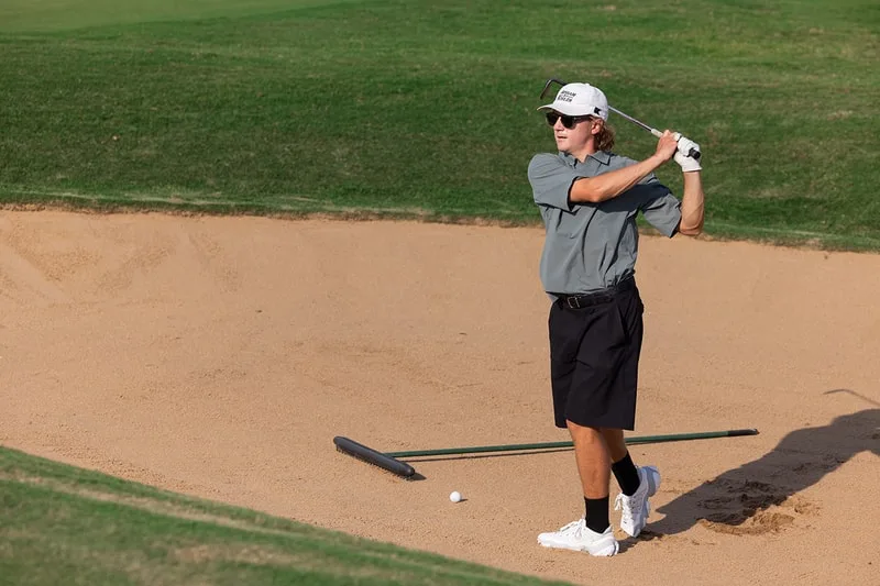 Joueur de golf en mouvement dans un bunker de sable sur le parcours.