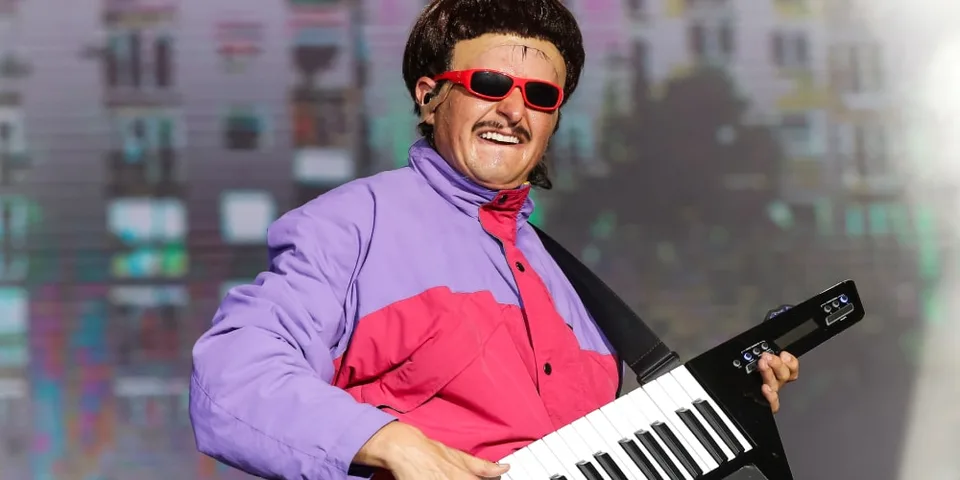 Personne en lunettes de soleil joue du synthétiseur-guitare sur scène.