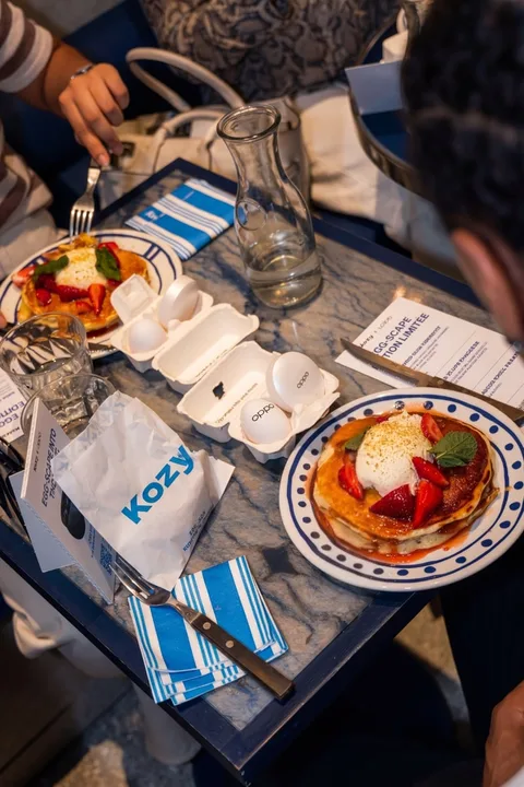 Deux plats de crêpes avec fruits et crème sur une table, serviette Kozys visible.