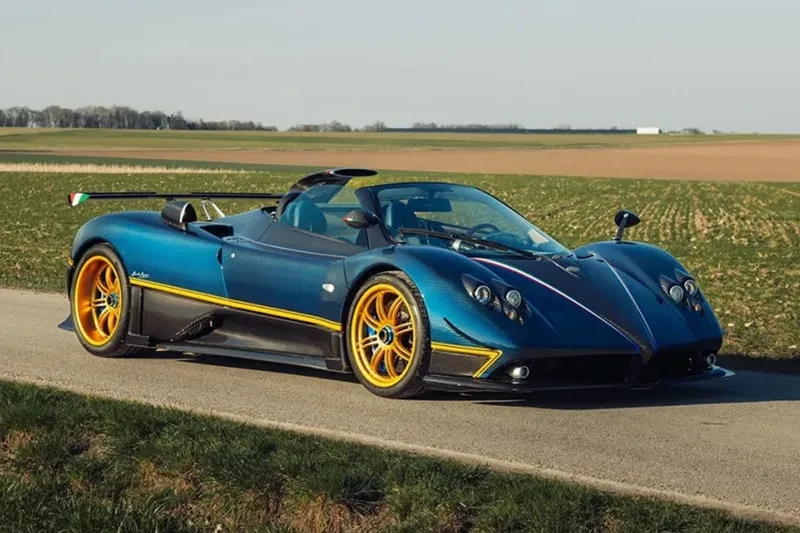 Voiture de sport bleue avec jantes dorées sur une route de campagne.