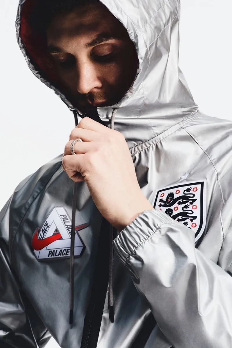 Personne portant une veste argentée avec logos Palace et badge football.