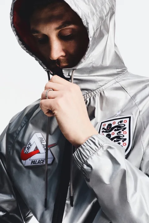 Personne portant une veste argentée avec logos Palace et badge football.
