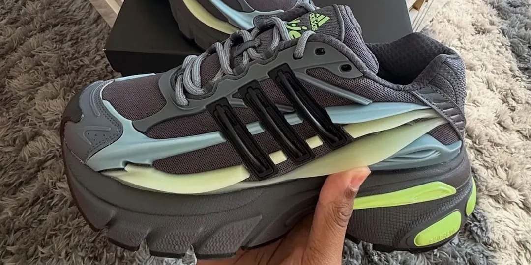 Chaussure de sport grise et verte avec détails noirs, tenue en main sur un tapis.