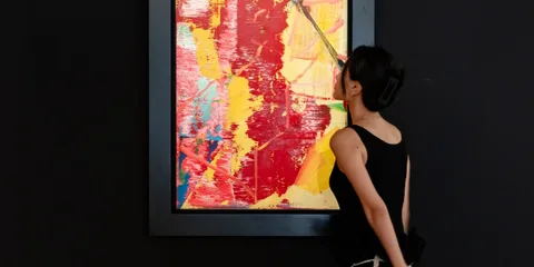 Femme en noir regarde une peinture abstraite aux couleurs vives dans un cadre.