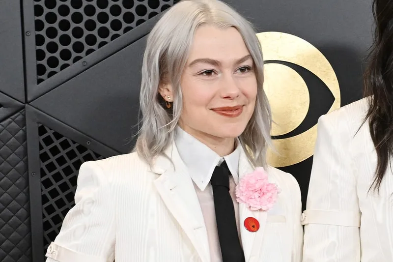 Personne en costume blanc avec fleur rose et cheveux gris.