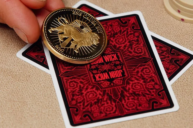 Main tenant une pièce sur deux cartes à jouer rouges, texte 'John Wick' visible