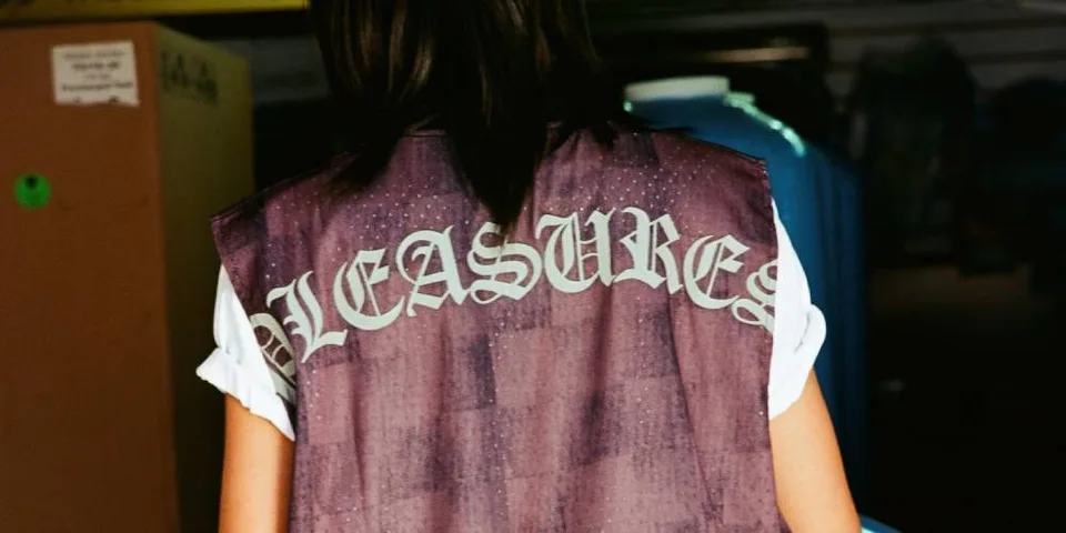 Personne portant un gilet avec 'PLEASURES' au dos.